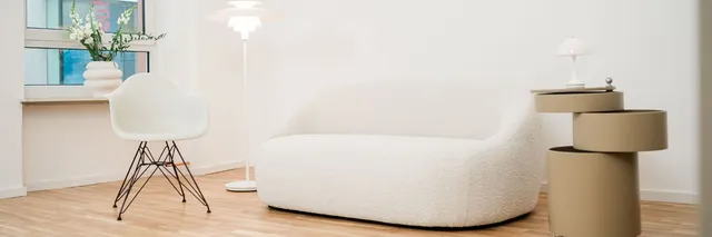 Wartebereich mit weißem Sofa, Schalensessel und Stehleuchte auf hellem Holzboden