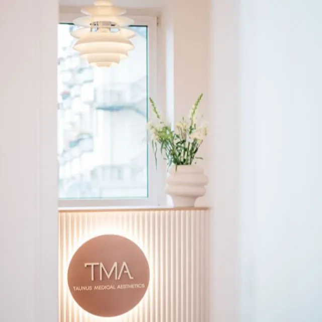 Beleuchtetes Praxislogo am Empfangstresen, daneben Fenster und Blumen
